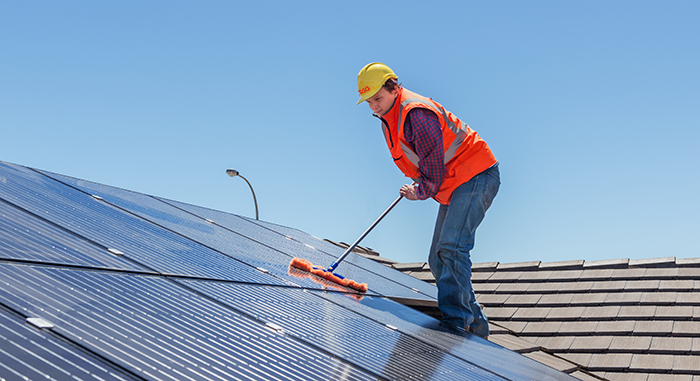 young worker cleaning solar panels on house roof